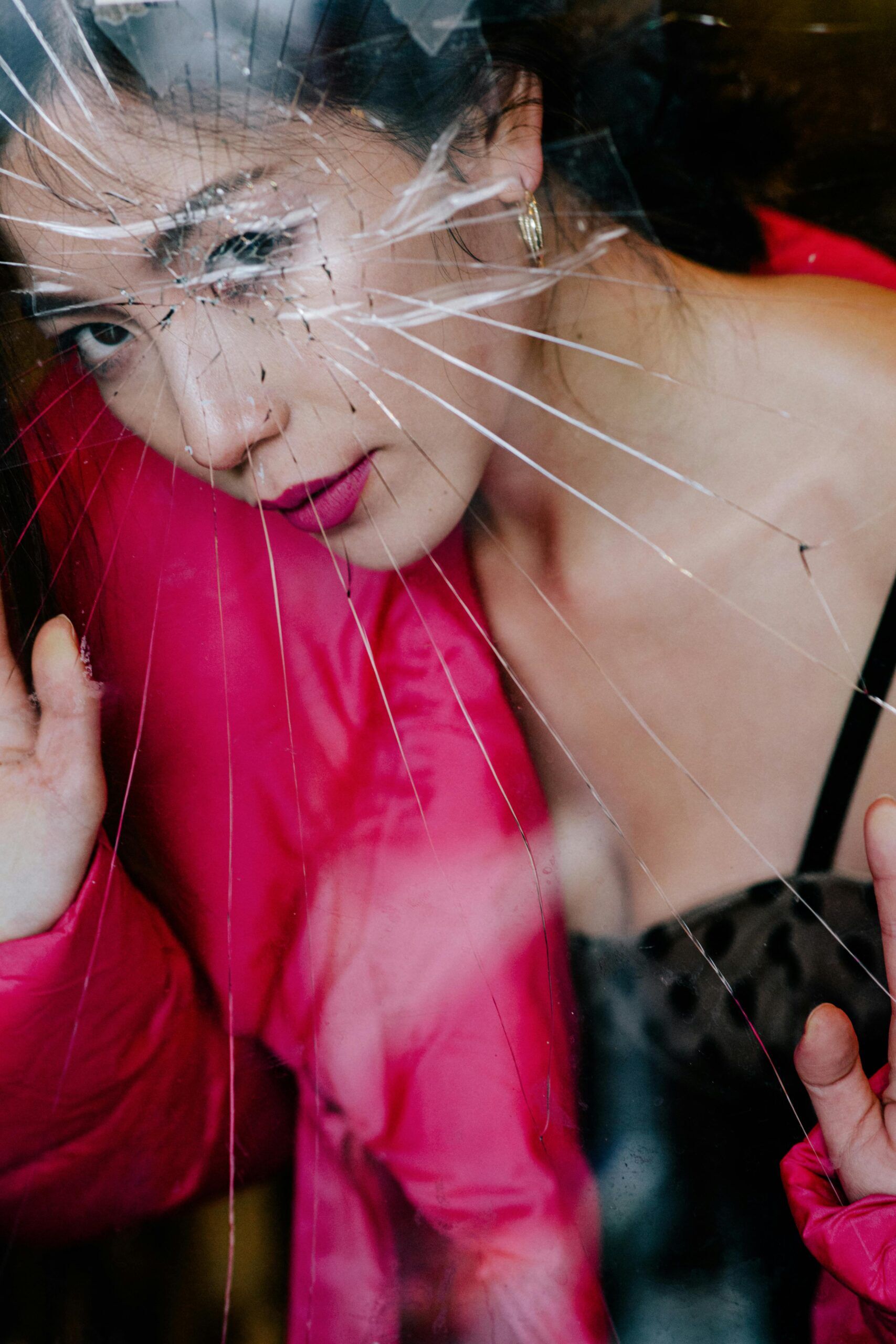 A stylish woman peers through shattered glass in a vibrant, contemplative pose.